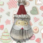 A Santa face folded out of a recycled book & decorated, on a background of Christmas cookies.