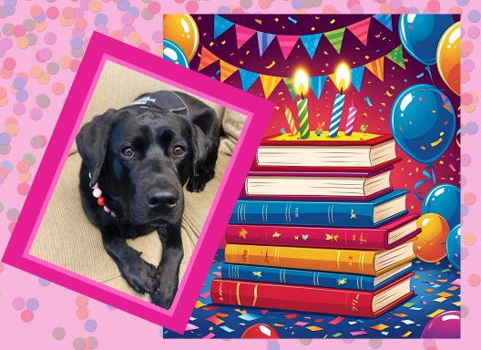 A black Labrador Retriever siting next to a stack of books with four birthday candles and balloons.